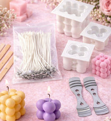 Candle-making supplies including molds, wicks, and candles on a pink surface with flowers.