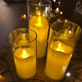 Three yellow candles in glass holders on a reflective surface with spider web decorations.