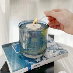 Hand lighting a candle in a decorative glass holder on a magazine