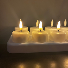 Row of lit tealight candles on a white holder against a dark background