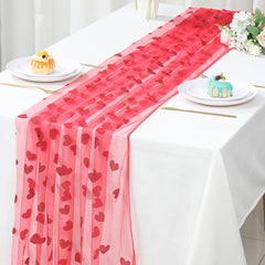 Table setting with a red heart-patterned table runner on a white tablecloth.