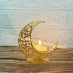 Decorative gold crescent moon candle holder with a lit candle on a wooden surface.