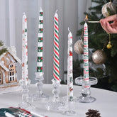 Decorative candles with Christmas designs on a table with a Christmas tree in the background.
