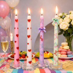 Decorative candles with heart and bow designs on a colorful table setting with flowers and balloons.