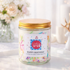 Candle with a 'Happy Birthday' label on a white surface with flowers in the background