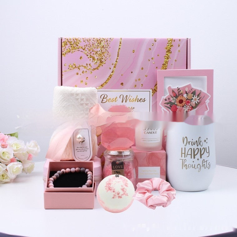 Collection of pink and white gift items including a mug, candle, and bath bomb on a white surface.