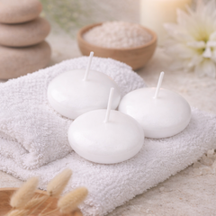 White floating candles on a towel with spa elements like stones and flowers in the background.