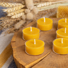 Yellow candles in glass holders on a wooden surface with wheat in the background