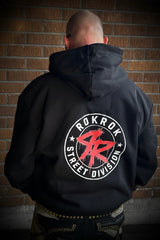 A man viewed from behind wearing a black pullover hoodie with a large circular back graphic that reads 'ROKROK STREET DIVISION' around a red stylized 'RR' logo, standing against a brick wall.