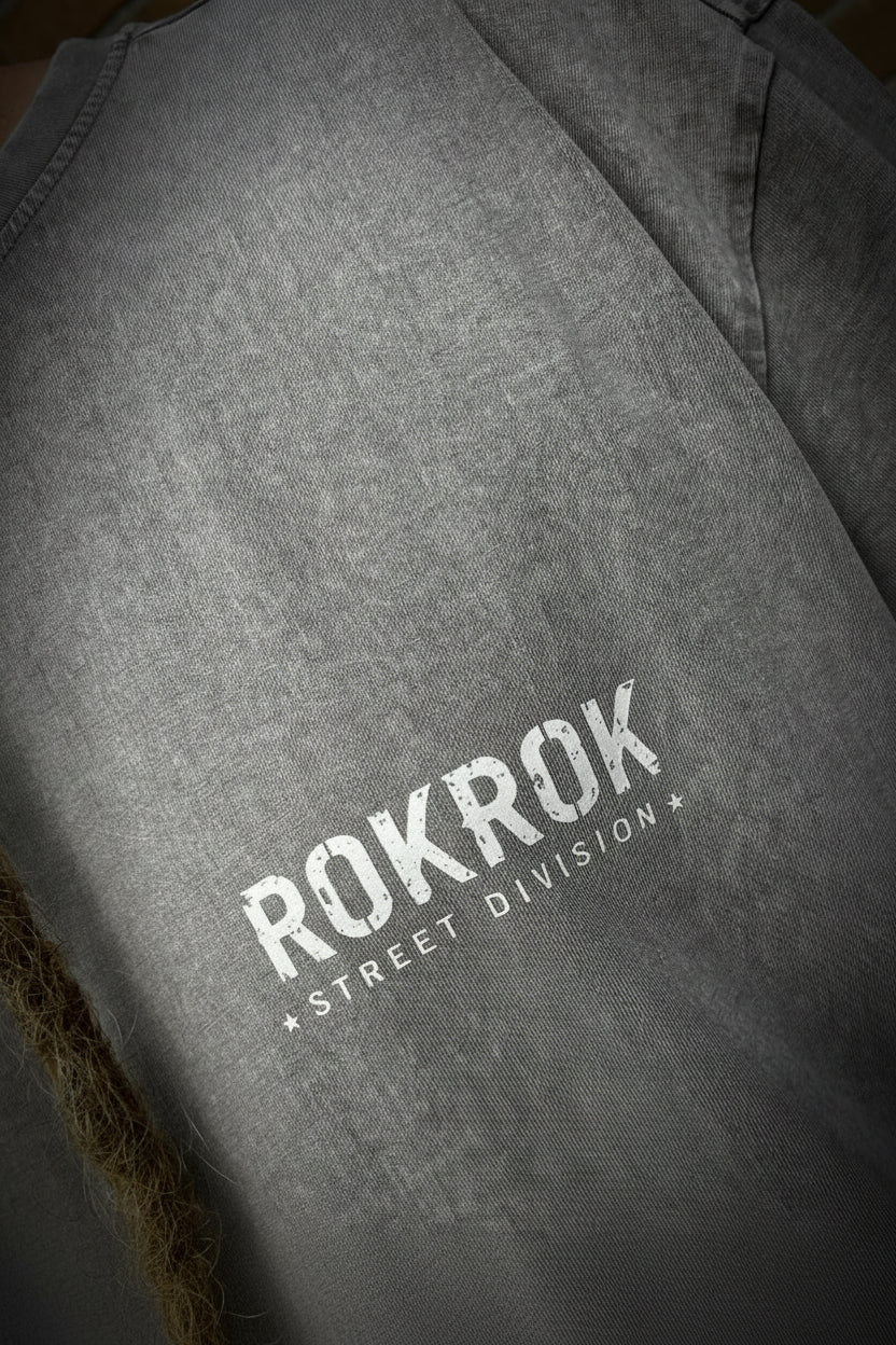 A close-up of a gray mineral-wash t-shirt featuring the text 'ROKROK STREET DIVISION' printed in white on the chest.