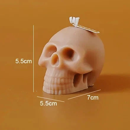 A small skull-shaped candle shown on a warm orange-brown background with printed dimensions (5.5 cm height, 5.