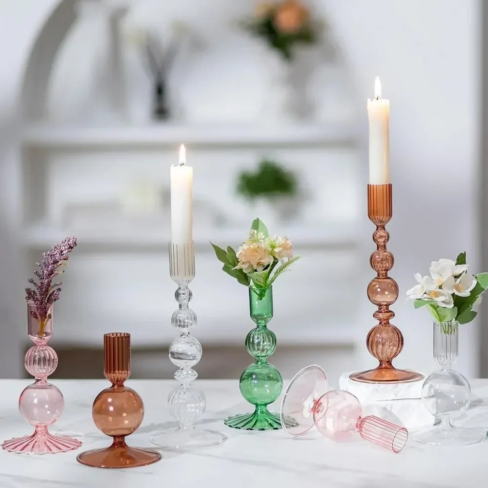 Set of colorful glass candle holders and vases on a white surface with a blurred indoor background.
