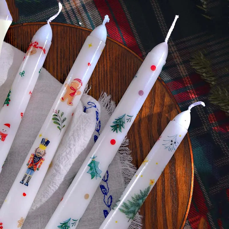Decorative candles with Christmas-themed illustrations on a wooden surface.