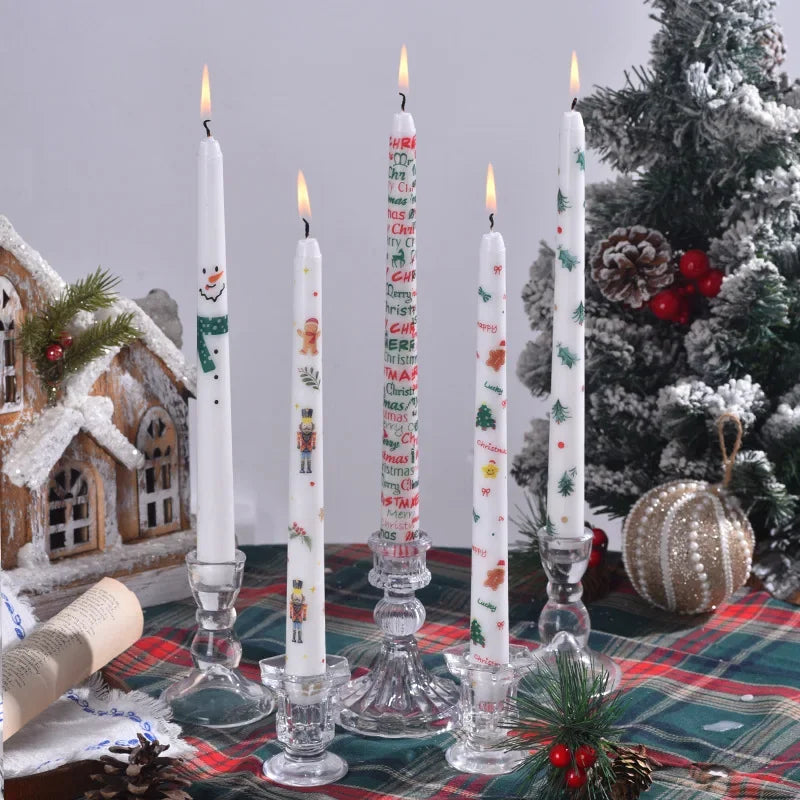 Set of Christmas-themed candles on a table with a decorated tree and gingerbread house in the background.