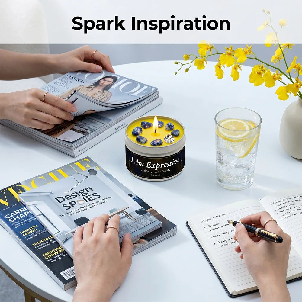Table with magazines, a candle, a glass of water, and a person writing in a notebook.