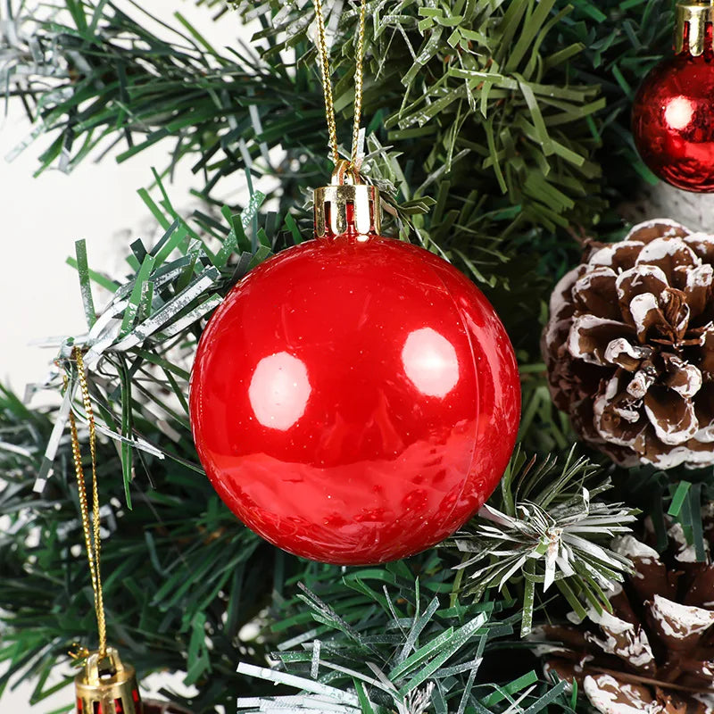 Red Christmas ball ornament hanging on a tree with pine cones and other decorations.