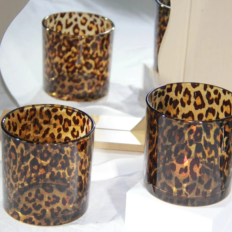 Three leopard print glass candle holders on a white surface.