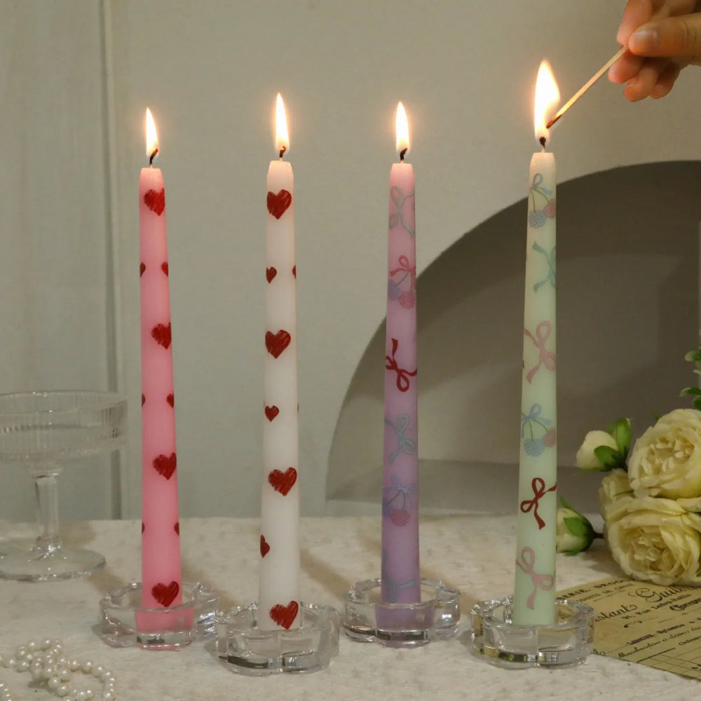 Four decorated candles on a table with a hand lighting one of them.
