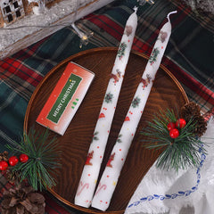 Two Christmas-themed candles on a wooden tray with decorative elements on a plaid fabric background.