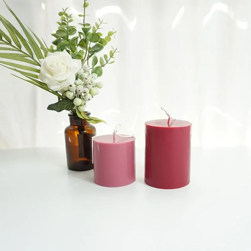 Two pink candles and a vase with flowers on a white surface