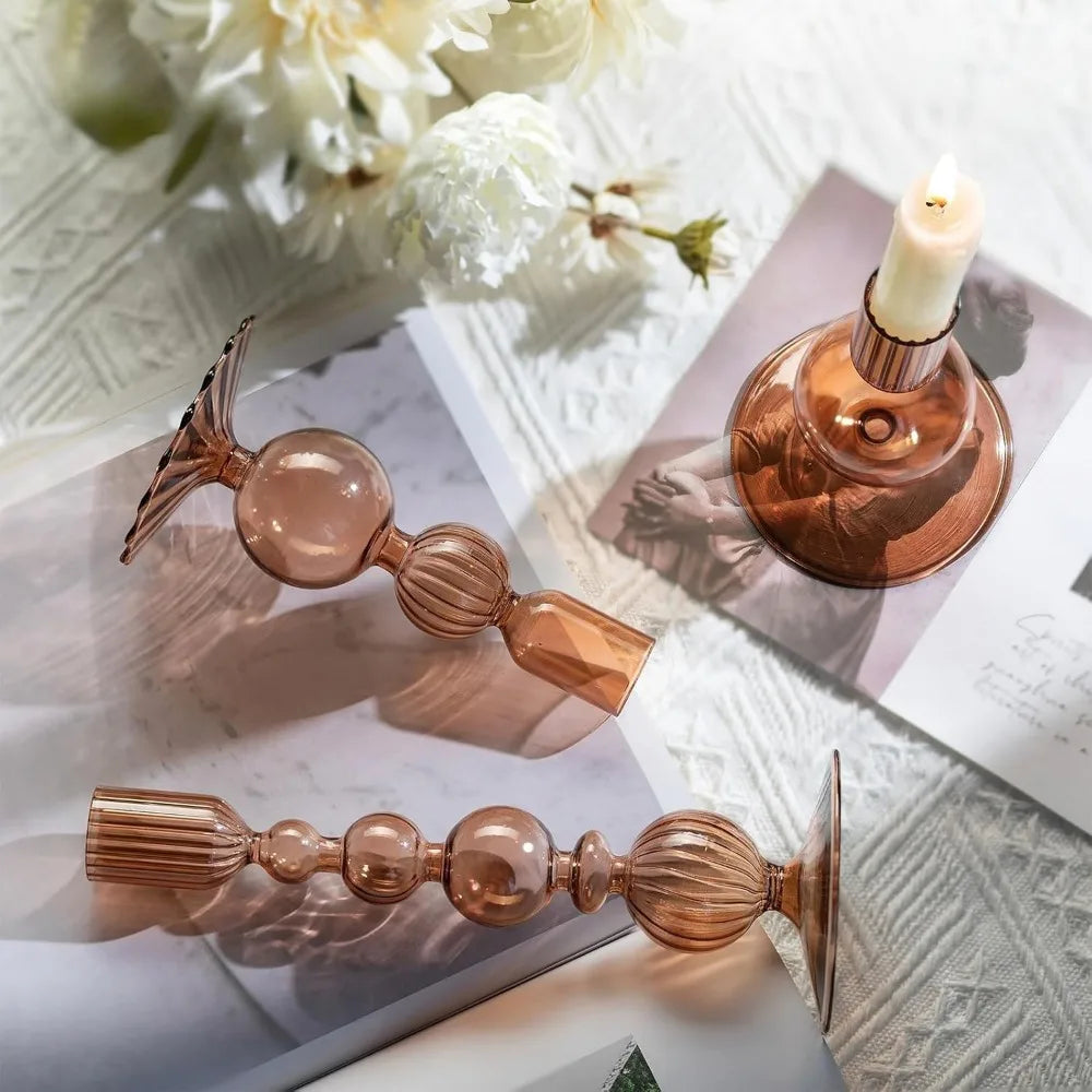 Decorative rose gold candle holders on a textured surface with flowers in the background