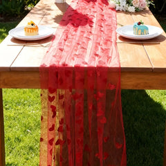 Red lace table runner on a wooden table with plates of cake outdoors.