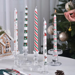 Decorative candles with Christmas designs on a table with a Christmas tree in the background.