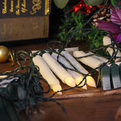 String lights with candles on a wooden surface, with a book and decorative items in the background.