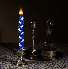 Blue and white braided candle with a silver holder on a dark background