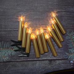 Set of gold candle-shaped string lights on a wooden surface with greenery.