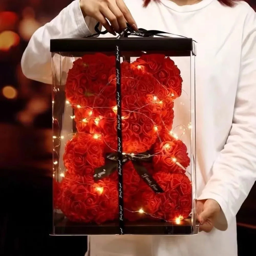 Red rose teddy bear with lights in a clear box held by a person.