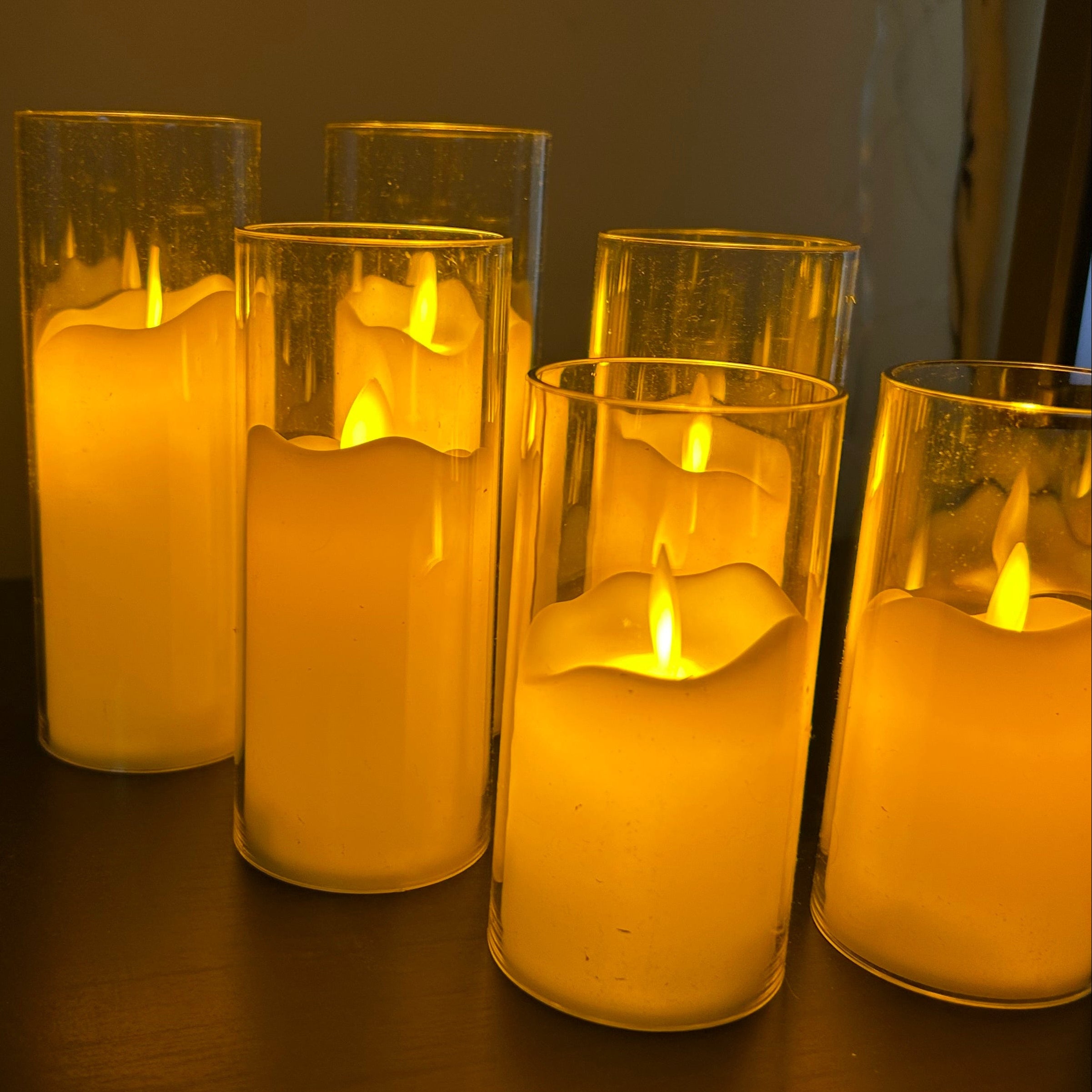Set of six lit candles in glass holders on a dark surface.