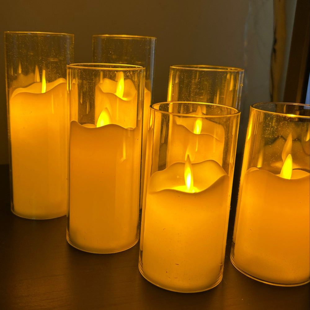 Set of six lit candles in glass holders on a dark surface.