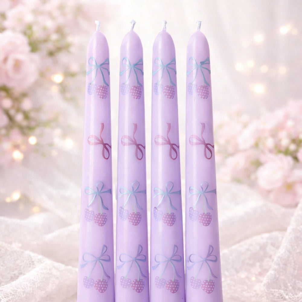 Four purple candles with decorative patterns on a soft, blurred floral background