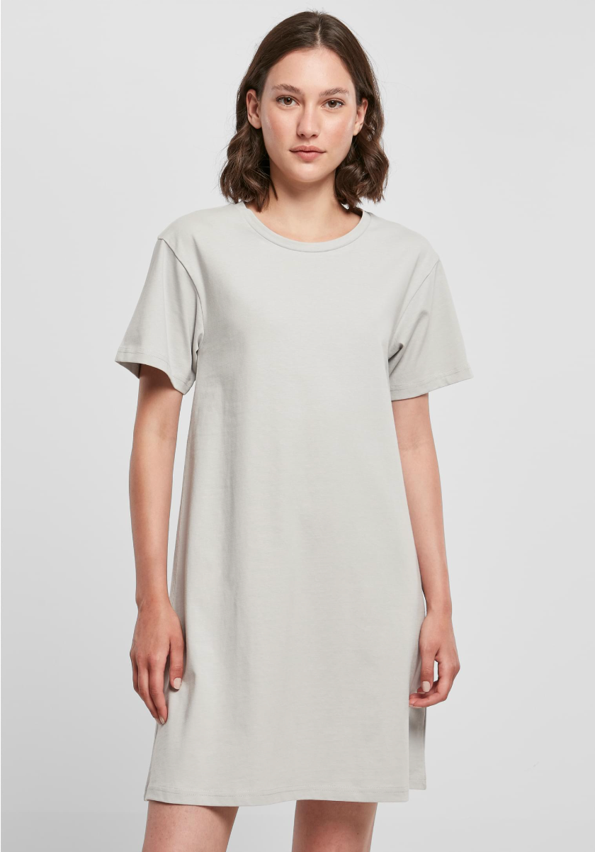 A woman modeling a light gray short-sleeve crewneck t-shirt dress against a plain light gray studio background.
